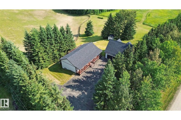 Aerial view of a house and garage surrounded by mature trees and adjacent to a green field. - 53203 Rge Road 15, Rural Parkland County