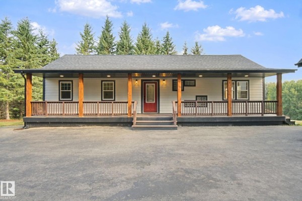 Front view of a single-story house with a wide covered porch, wooden railings, and a red front door. - 53203 Rge Road 15, Rural Parkland County