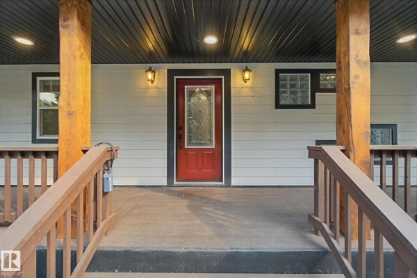 View from the steps leading to the front door, showing wooden porch columns, railings, and a red door. - 53203 Rge Road 15, Rural Parkland County