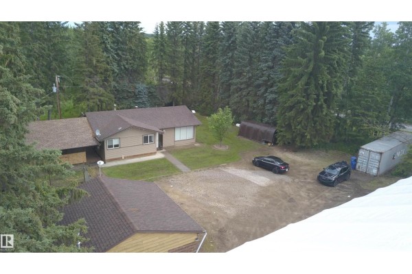 Aerial view of a residential property surrounded by tall trees with two cars parked outside. - 53212 Rge Road 14, Rural Parkland County