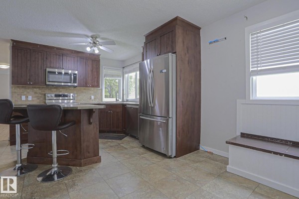 Kitchen with dark wood cabinets, stainless steel appliances, and a breakfast bar with stools. - 53212 Rge Road 14, Rural Parkland County