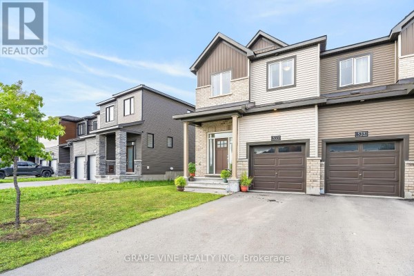 Side view of a townhouse complex with a driveway and green lawn in the foreground. - 533 Winterset Road, Ottawa