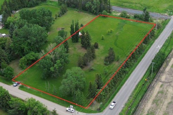Aerial view of a rural property with a red boundary line, showing trees, a small white building, and a paved road. - 53371 Rge Road 231, Rural Strathcona County