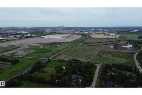 Distant aerial view of industrial buildings and fields, with a small cluster of trees in the foreground. - 53371 Rge Road 231, Rural Strathcona County