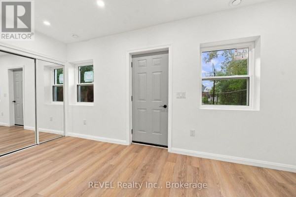 Interior of a room with white walls, wood-look flooring, a grey door, and a mirrored closet. - 533a Carlton Street, St  Catharines