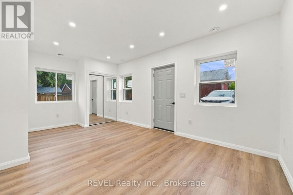 Interior of a room with white walls, wood-look flooring, a grey door, and a mirrored closet. - 533a Carlton Street, St  Catharines