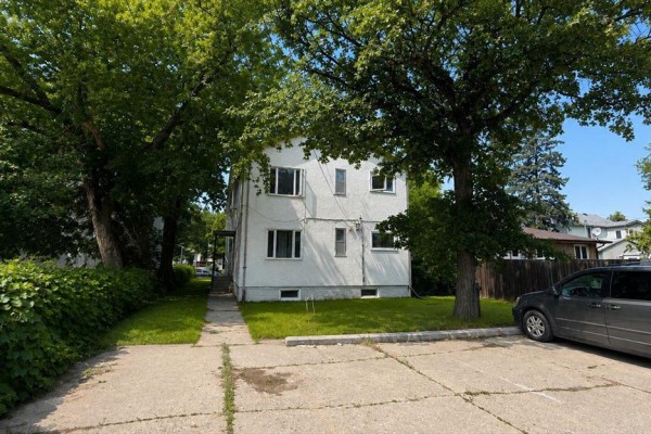 Back view of a white multi-family house surrounded by mature trees. - 534 Ritchot Street, Winnipeg