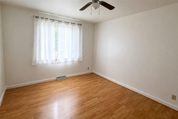 Empty room with light wood laminate flooring, white walls, and a ceiling fan. - 534 Ritchot Street, Winnipeg