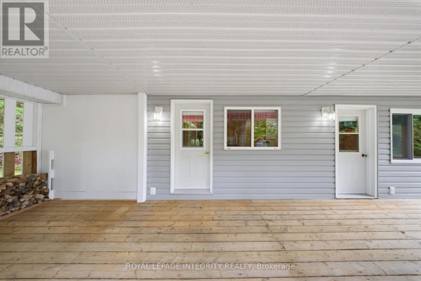 Covered porch with wood flooring, showing two doors, a window, and stacked firewood. - 534 School House Lane, Greater Madawaska