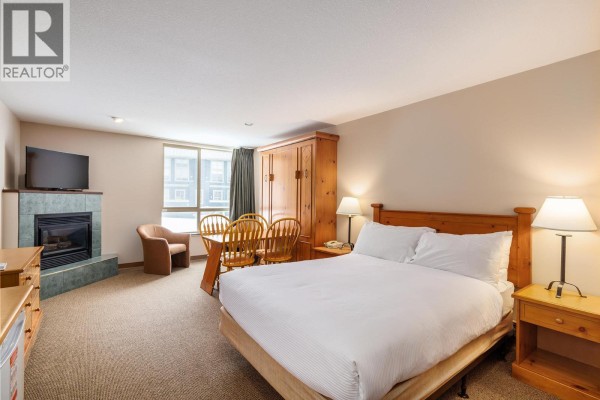 Another angle of the studio apartment featuring a queen bed and dining area with chairs. - 5340 Big White Road Unit# 219, Big White