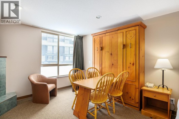 Dining area with a wooden table, chairs, and a cozy armchair by the window. - 5340 Big White Road Unit# 219, Big White
