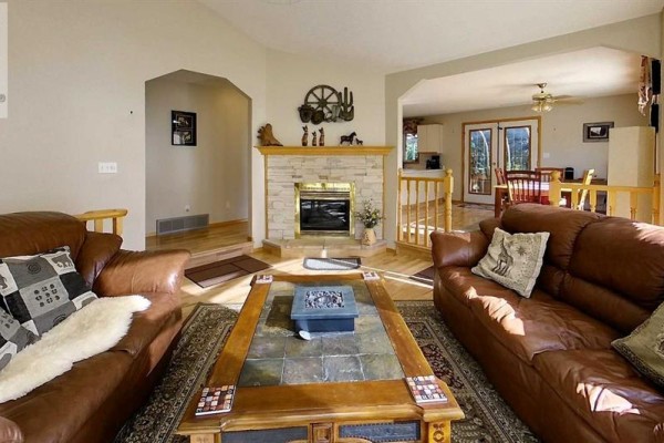 Living room featuring a stone fireplace, two leather sofas, and a view into the dining area. - 53419a Range Road 161, Rural Yellowhead County