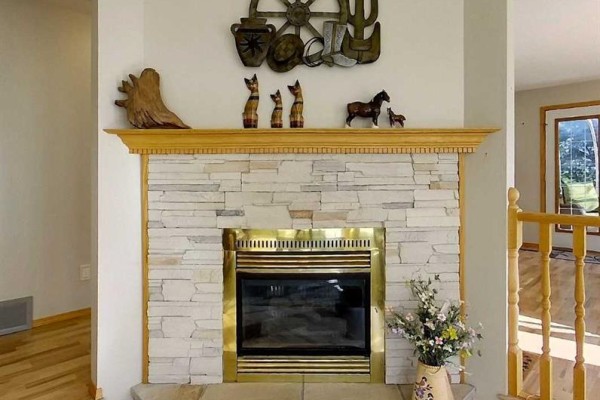 Close-up of a stone fireplace with a brass surround and decorative wooden items on the mantle. - 53419a Range Road 161, Rural Yellowhead County