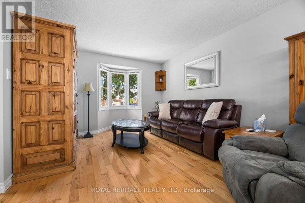 Living room with a leather sofa, armchair, bay window, and wooden armoire. - 535 Cardinal Drive, Peterborough
