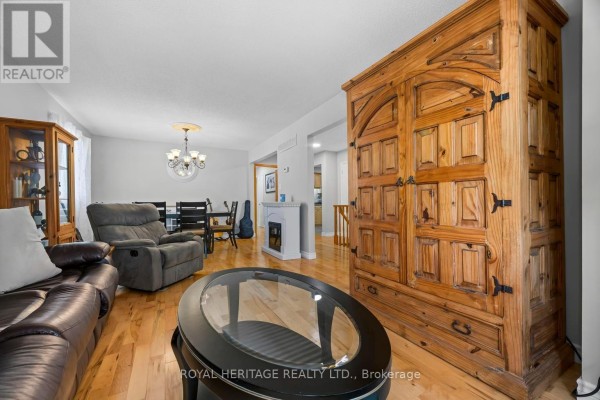 Living and dining area with a large wooden armoire, sofa, dining table, and fireplace. - 535 Cardinal Drive, Peterborough