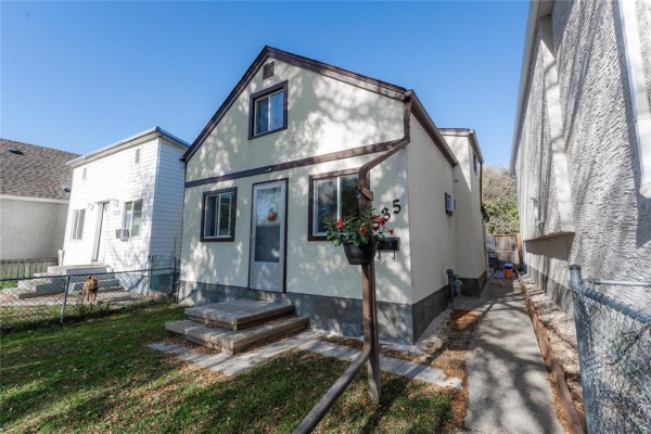 Side exterior view of a light-colored house with a driveway, lawn, and fence. - 535 Jamison Avenue, Winnipeg