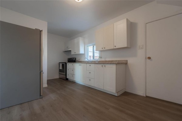 Kitchen with white cabinets, stainless steel refrigerator, and light wood-look flooring. - 535 Jamison Avenue, Winnipeg