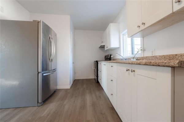 Kitchen with white cabinets, granite countertops, stainless steel appliances, and light wood-look flooring. - 535 Jamison Avenue, Winnipeg