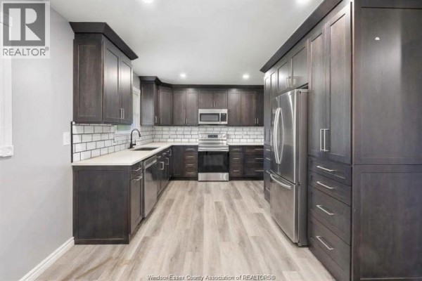 Modern kitchen with dark wood cabinets, white subway tile backsplash, stainless steel appliances, and light wood-look flooring. - 536 Mersea Rd 3, Leamington