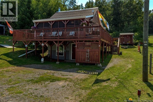 Side view of a wooden cottage with a large deck, screened porch, and attached storage. - 5364 Route 102, Hampstead
