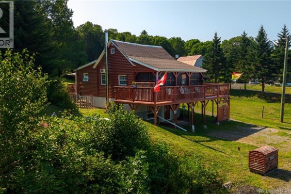 Side view of a red wooden cottage showing the side deck and screened-in porch. - 5364 Route 102, Hampstead