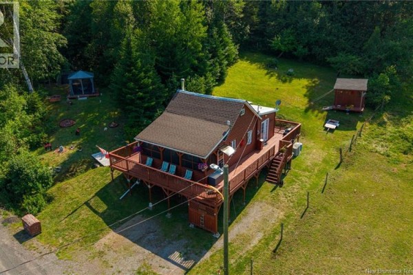 Aerial view of a red wooden cottage surrounded by green trees and a large wooden deck. - 5364 Route 102, Hampstead