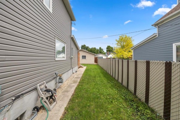 Side view of a grey house with a narrow grassy pathway and a fence. - 537 Cherrier Street, Winnipeg