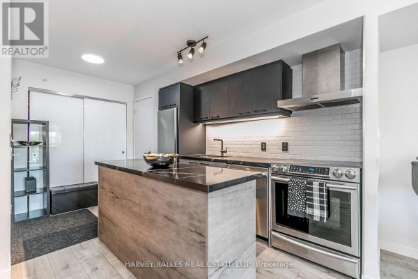 Modern kitchen with black countertops, grey cabinets, stainless steel appliances, and a wood-grain island. - 538 - 68 Abell Street, Toronto