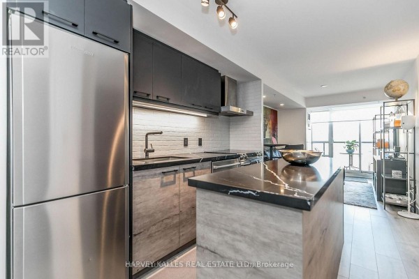 Open concept kitchen and living area with a stainless steel refrigerator, grey cabinets, and island. - 538 - 68 Abell Street, Toronto