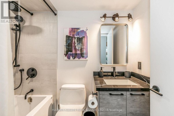 Compact bathroom with a white bathtub, toilet, vanity, and black fixtures. - 538 - 68 Abell Street, Toronto