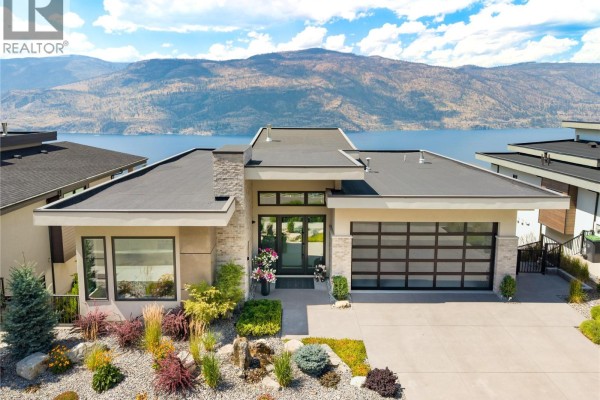 Front exterior of a modern house with a stone facade, glass garage door, and manicured front yard. - 538 Clifton Court, Kelowna