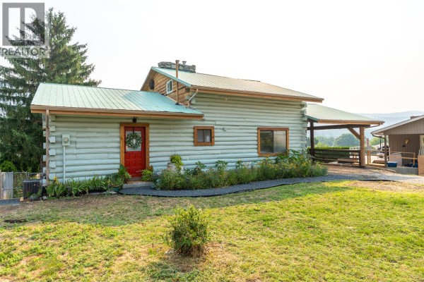 Exterior of a light blue log home with a red front door and a covered carport on the right side. - 538 Lakeview Place, Oliver