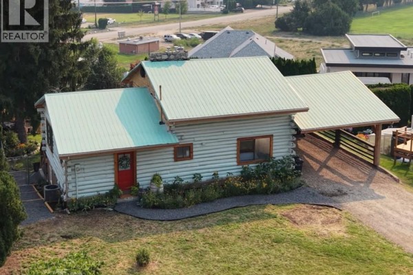 Aerial view of a light blue log home with a red door and a green metal roof, set in a grassy yard. - 538 Lakeview Place, Oliver
