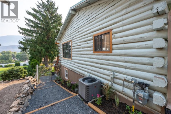 Close-up of the light blue log siding of a house, with a window, AC unit, and gas meter visible. - 538 Lakeview Place, Oliver