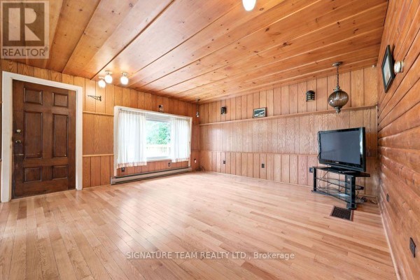 Living room with wood-paneled walls, hardwood floors, a large window, and a television on a stand. - 538 Lenser Road, Bonnechere Valley