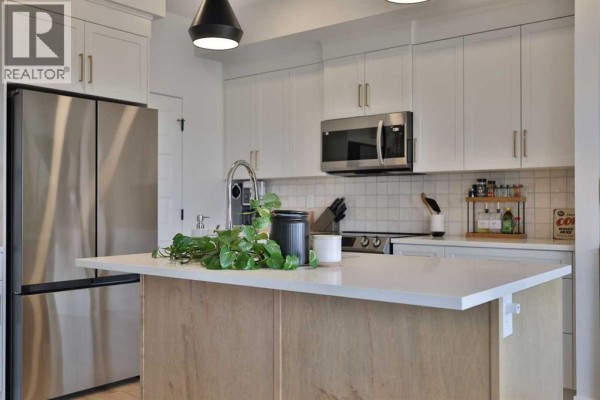 Kitchen with white cabinets, subway tile backsplash, stainless steel appliances, and an island. - 538 Malahat Green W, Lethbridge