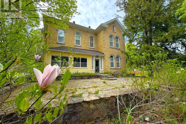View of a large yellow brick house from across a green lawn with mature trees. - 538 Queen Street N, Arran Elderslie