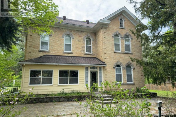 Front exterior of a two-story yellow brick house with arched windows and a covered porch. - 538 Queen Street N, Arran Elderslie