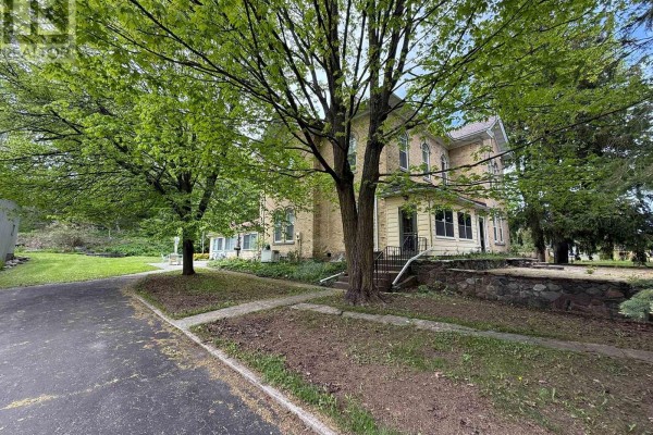 Driveway leading to the side entrance of a yellow brick house surrounded by trees and stone landscaping. - 538 Queen Street N, Arran Elderslie