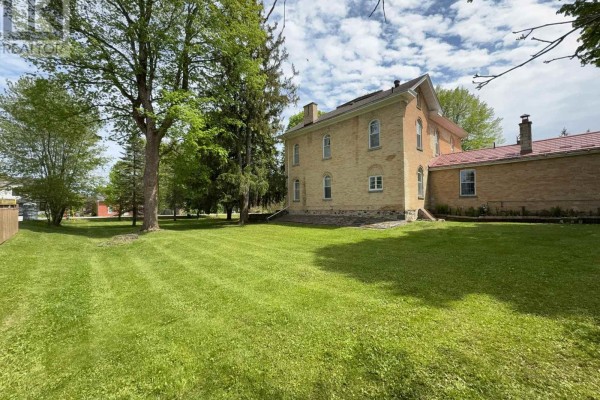 Rear view of a yellow brick house with a large green lawn and mature trees. - 538 Queen Street N, Arran Elderslie