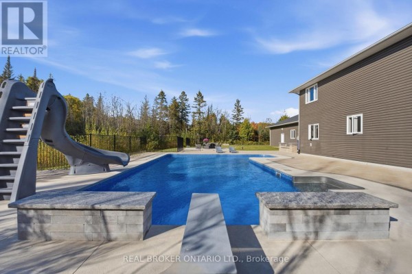 A rectangular swimming pool with a slide and integrated hot tub on a paved patio beside a grey house. - 5381 Desmarais Road, Greater Sudbury