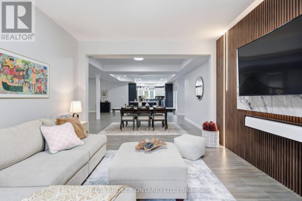 Living room with light grey walls, wood slat accent wall, and an open view to a formal dining area and kitchen. - 5381 Desmarais Road, Greater Sudbury