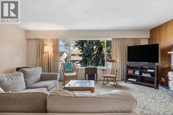 Living room with beige carpet, a large window, and a gray sectional sofa. - 5392 Maple Crescent, Delta