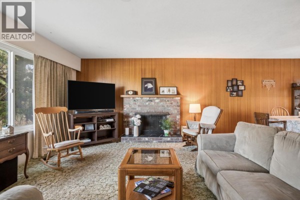 Living room with wood-paneled walls, a brick fireplace, and seating. - 5392 Maple Crescent, Delta