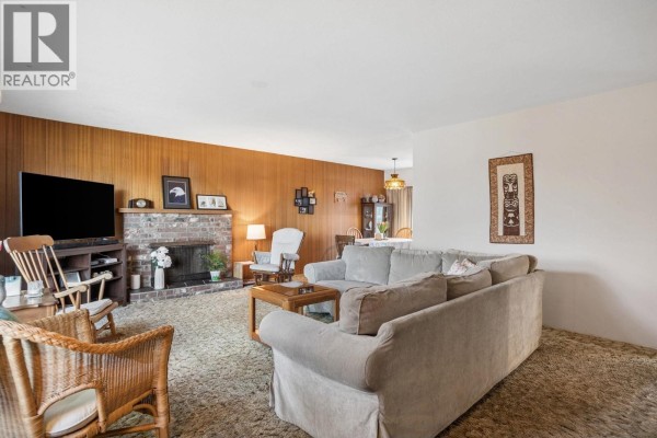 Living room with beige carpet, wood-paneled walls, and a large gray sofa. - 5392 Maple Crescent, Delta