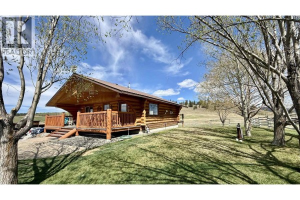 Living room featuring stone fireplace, large windows, and comfortable seating - 5393 Tatton Station Road, 100 Mile House