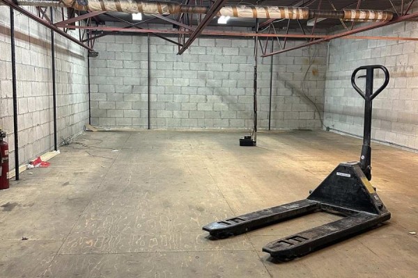 Empty warehouse space with concrete block walls, wooden floor, and pallet jack. - 54 - 173 Advance Boulevard, Brampton