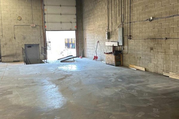 Interior view of warehouse with open garage door, concrete floor, and cinder block walls. - 54 - 173 Advance Boulevard, Brampton