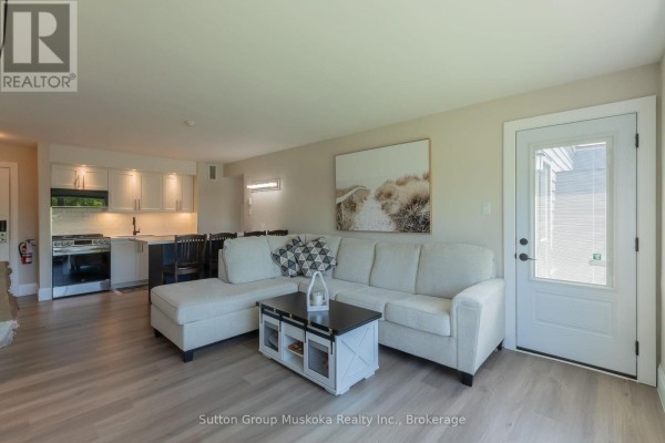 Living room with a sectional sofa, coffee table, and view of the kitchen. - 54 - 54-305 Deerhurst, Summit Lodge Drive, Huntsville