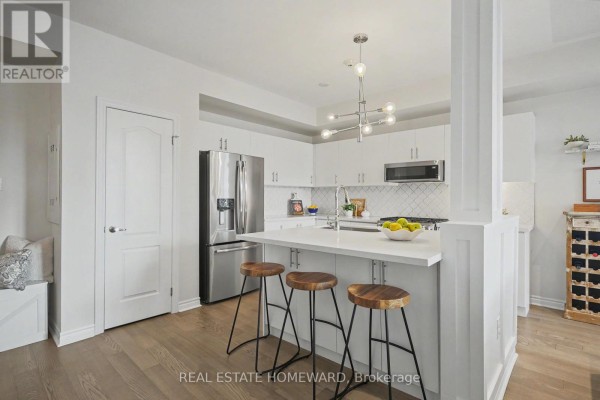 Kitchen with stainless steel appliances, island with stools, and entryway bench. - 54 - 57 Armdale Road, Mississauga